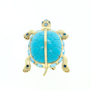 TORTUGA - TORTUGA è una spilla a forma di tartaruga da indossare sempre per richiamare la buona sorte. È un gioiello realizzato in oro chiaro con resina color acquamarina, strass zaffiro e acquamarina. - A.Z. Bigiotterie